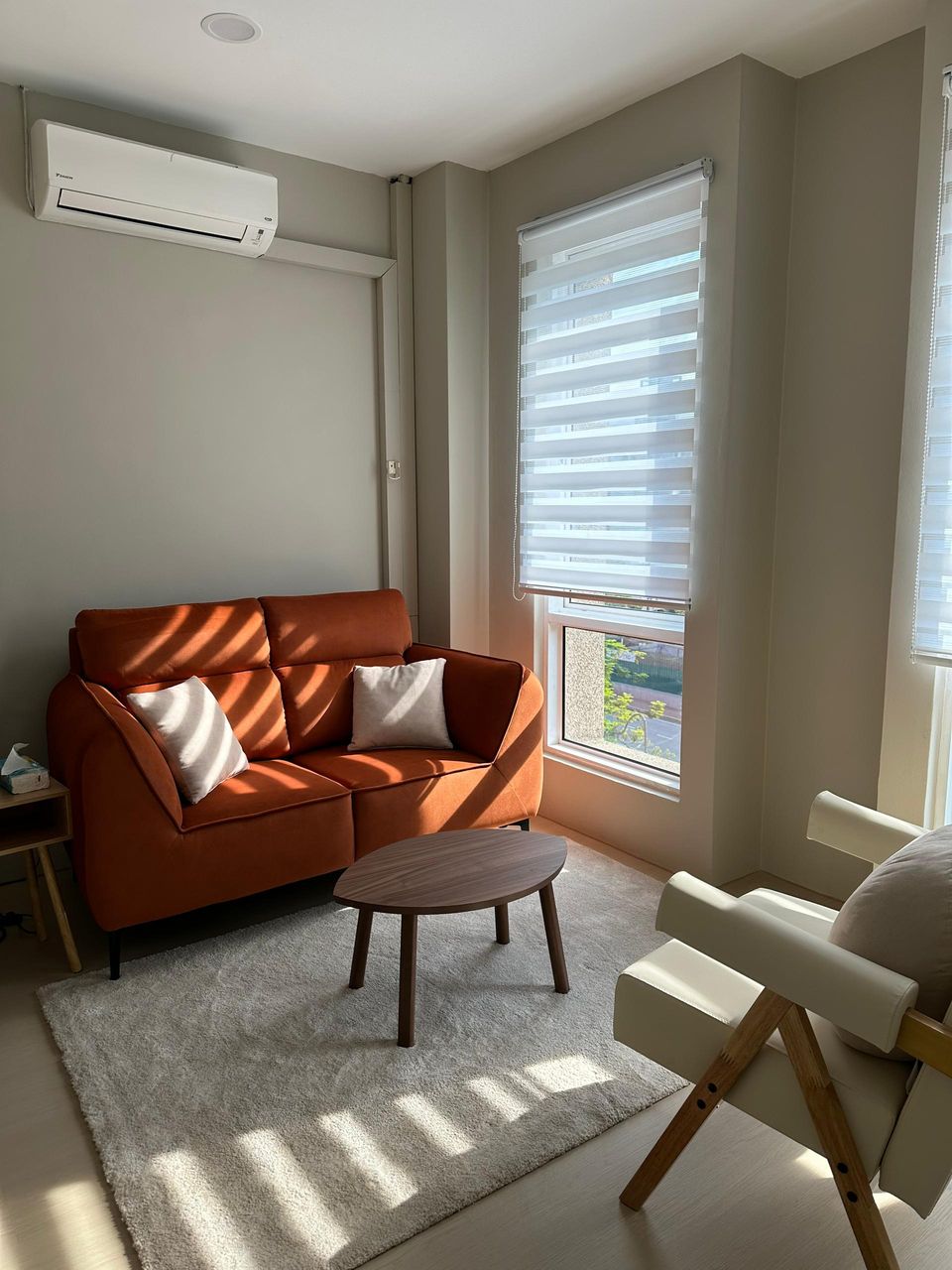 The Beige Room in afternoon light, with the rust-orange sofa, an armchair and a round table