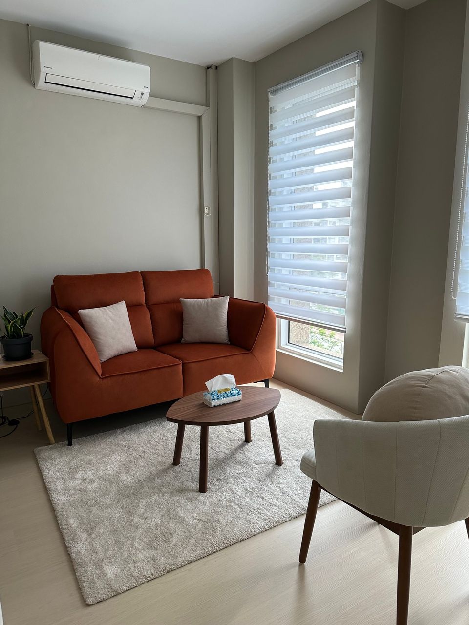 The Beige Room: a rust-orange sofa by the window, a round wooden table and a cream armchair