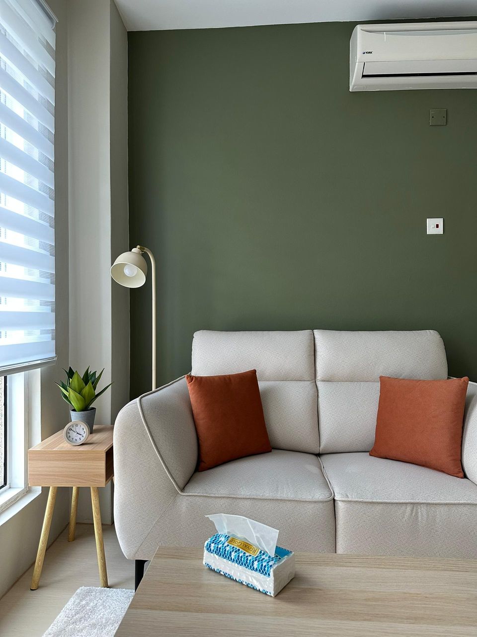 The Olive Room sofa with orange cushions against the olive-green wall, beside a floor lamp